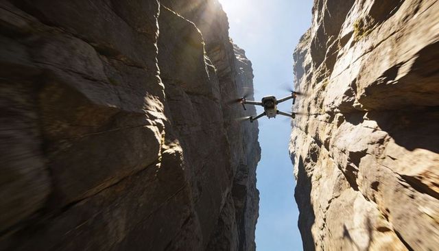 Quadcopter navigating narrow slot canyon between towering sandstone cliffs with sun flare