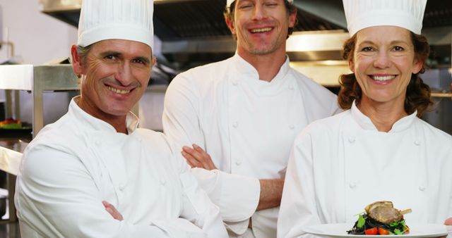 Chefs in white uniforms standing together in a restaurant kitchen, smiling and displaying camaraderie. This could be used in articles or advertisements related to culinary arts, professional kitchen environments, team collaboration in restaurants, or culinary training courses.