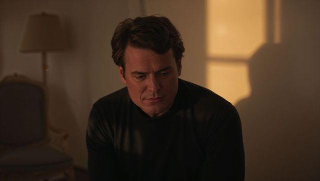 Pensive man sitting in warm window light, gazing downward — contemplative interior portrait