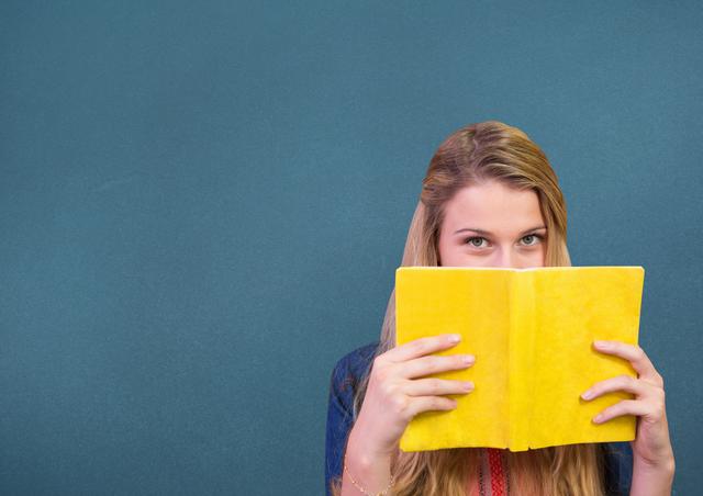 Woman holding a book in front of her face against blue background
