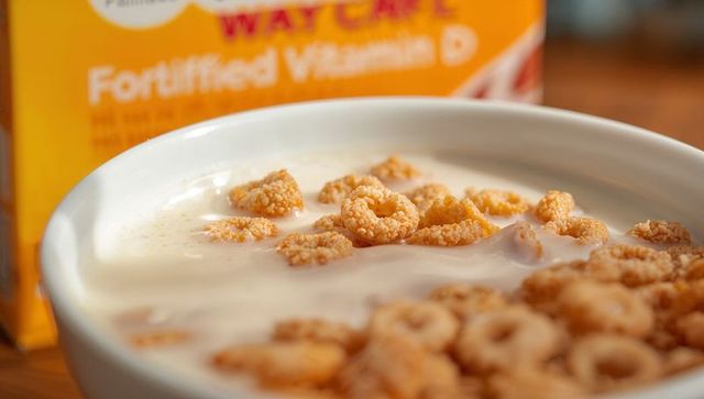 Macro close-up of oat ring cereal soaking in milk with blurred fortified box