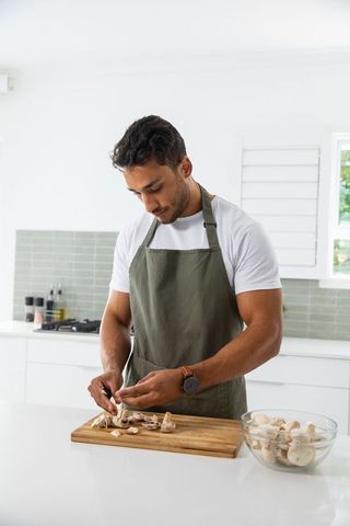 Man in Olive Apron Preparing Mushrooms in Modern Kitchen