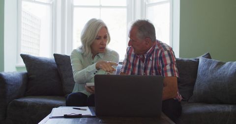 Senior Couple Reviewing Finances with Laptop on Sofa at Home