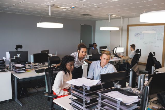 Business colleagues collaborating at a desk in a modern office. Ideal for illustrating teamwork, corporate environments, professional discussions, and productivity in a diverse workplace. Suitable for business presentations, corporate websites, and articles on office culture.