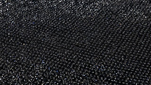Macro glittering black bead texture on dark fabric, sparkling granular shimmering pattern