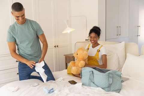 African american couple packing weekend bag together on cozy bright bedroom bed