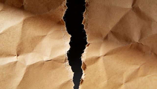 Close-up torn kraft paper revealing black gap macro texture frayed fibers creases crumpled tan sheet
