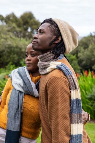 African american couple embracing outdoors in park wearing scarves, beanie, autumn fashion