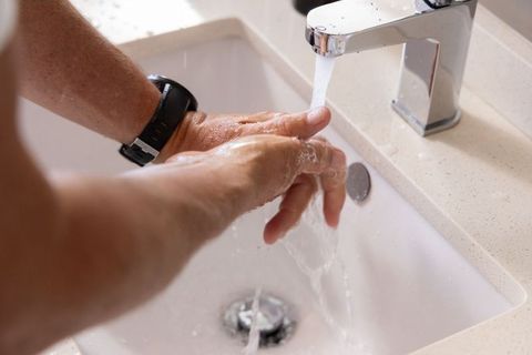Man rinsing hands under chrome faucet at bathroom sink wearing black wristwatch