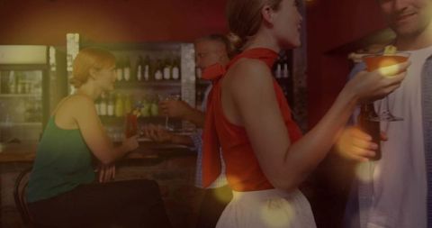 Woman clinking cocktail glass at cozy lounge bar with warm bokeh lights and evening social