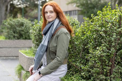 Redheaded woman sitting on planter in urban courtyard wearing scarf and jacket