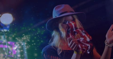 Female singer wearing fedora shaking tambourine under colorful stage lights