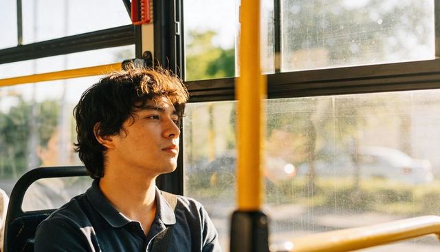 Young commuter gazing out sunlit bus window, urban transit lifestyle, reflective moment