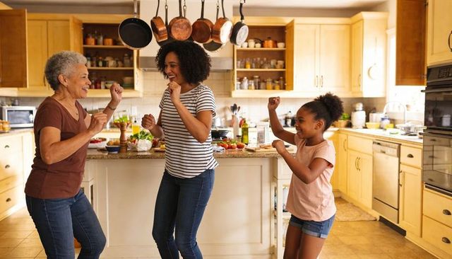 Multigenerational joyful family dancing in sunlit kitchen preparing meal with fresh produce
