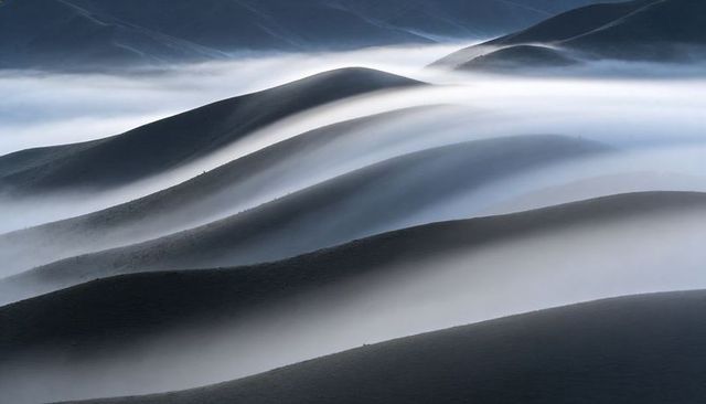 Undulating ridgelines weaving through low fog, minimalist moody hills at dawn