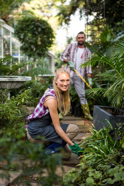 This image depicts a happy young female gardener working in a lush community garden alongside a colleague. Ideal for use in articles or advertisements related to gardening, community projects, teamwork, environmental sustainability, and outdoor activities.