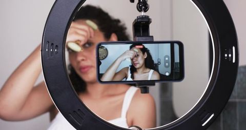 African-american creator recording skincare routine with facial roller and ring light
