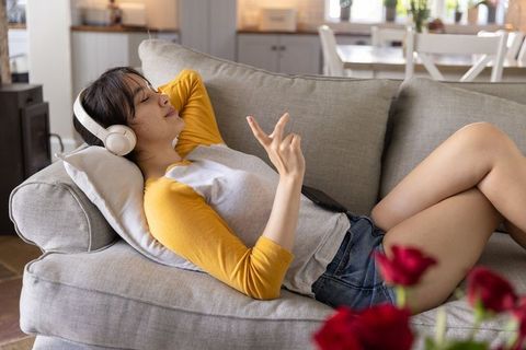 Young asian woman relaxing on sofa with headphones and smartphone in cozy home interior