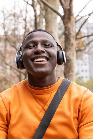 Smiling young man listening to music on over-ear headphones while commuting in urban park