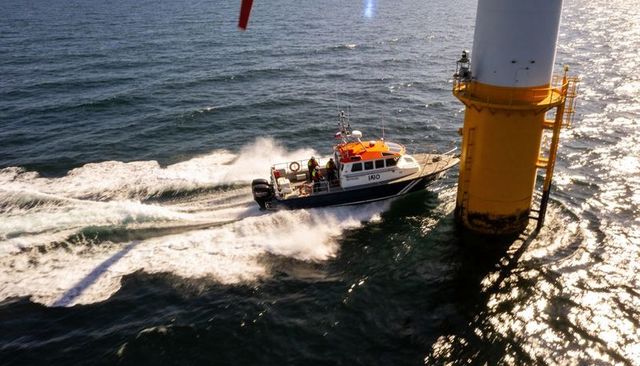 Rescue vessel speeding and cutting wake beside offshore wind turbine monopile at sunset