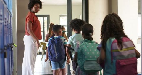 Teacher guiding young students through school hallway with backpacks and lockers