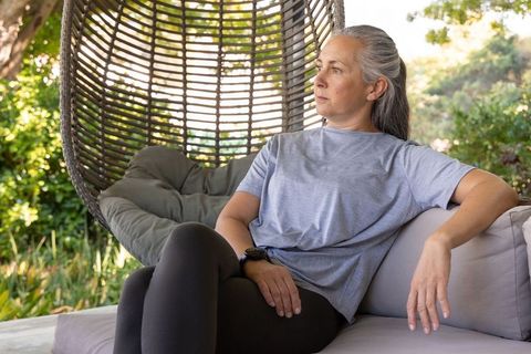 Mature woman relaxing on outdoor wicker egg chair, contemplative garden patio moment