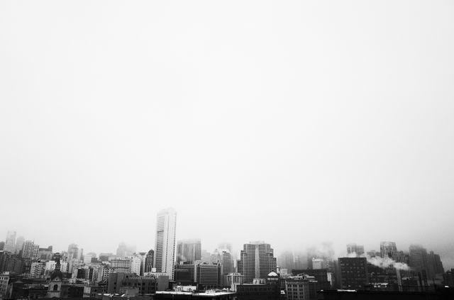 Monochrome city skyline with buildings and rooftops visible under a layer of fog, creating an atmospheric urban setting. Perfect for use in projects related to city life, urban exploration, business, weather, and atmosphere. Great for posters, blogs, websites focusing on cityscapes, modern architecture, or metropolitan living.