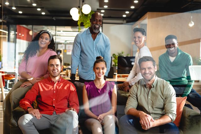 This picture shows a group of happy, diverse business people posing together in a modern office. They are smiling, representing teamwork, cooperation, and a positive work environment. This image can be used to represent diversity, inclusion, and collaboration in professional settings, as well as for promotions of workplace culture and group dynamics in business environments.