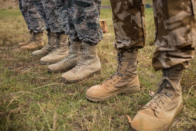 Low-section view of military soldiers standing in line wearing various camouflaged uniforms and boots. Ideal for use in articles about military training, teamwork, discipline, and the life of soldiers. Can also be used for recruitment advertisements or military-themed publications.
