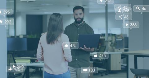 Scene depicting a business discussion where a man's use of a laptop promotes social media engagement with icons symbolizing likes and interactions. Ideal for illustrating digital marketing concepts, data-driven decision-making in modern businesses, and teamwork dynamics in corporate settings.