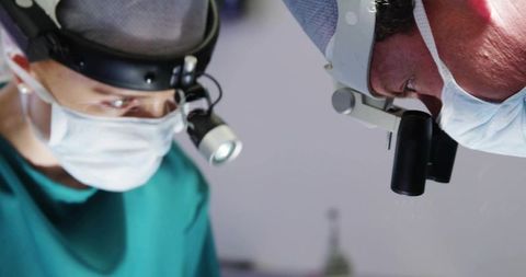 Two surgeons leaning over patient performing delicate surgery with headlamps and loupes