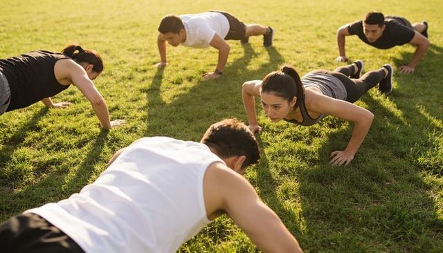 Group doing outdoor push-ups at golden hour, focused team fitness training on grass