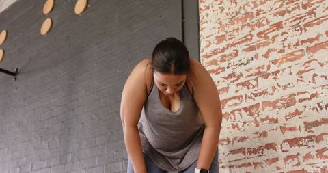 Woman leaning forward after intense workout in industrial gym with brick wall