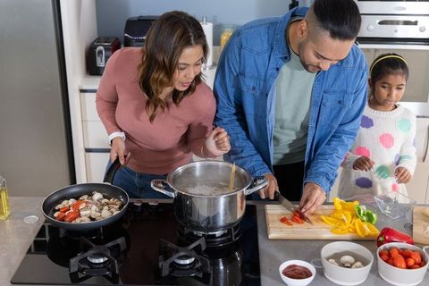 Family cooking together on kitchen island, parents chopping vegetables while child watching