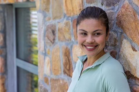 Smiling woman leaning on stone wall wearing mint zip-up casual outdoor portrait