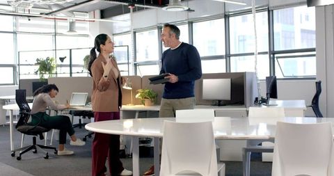 Diverse colleagues discussing and collaborating in modern open-plan office with tablet