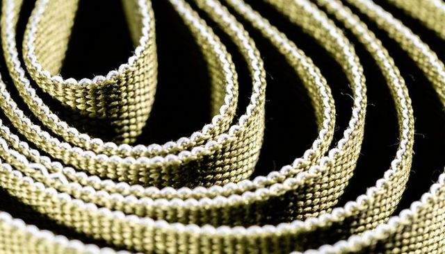 Coiled olive green nylon webbing macro showing woven texture spiral pattern loose fibers