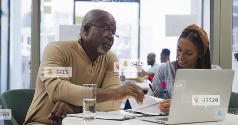 Senior professional mentoring young colleague over laptop, reviewing documents and collaborating