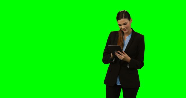 An image of a businesswoman in a dark suit using a tablet against a bright green screen background. This image is ideal for presentations, advertisements, or instructional materials that require the insertion of different backgrounds or approaches for remote work, corporate activities, or business tech usage illustrations.