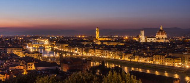 This scenic urban panorama captures Florence during the evening, radiating a golden glow from illuminated historic buildings, including Florence Cathedral and Ponte Vecchio. Ideal for promoting tourism, travel blogs, architectural reviews, cultural documentation, and travel agencies.