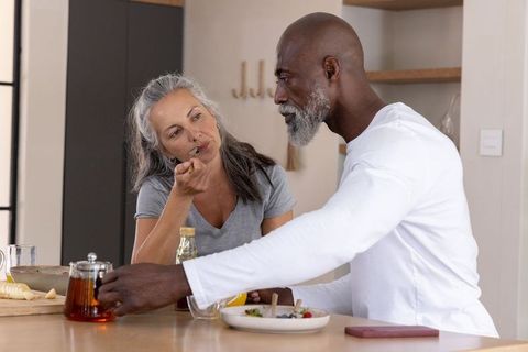 Mature diverse couple tasting breakfast at kitchen island, cozy morning routine