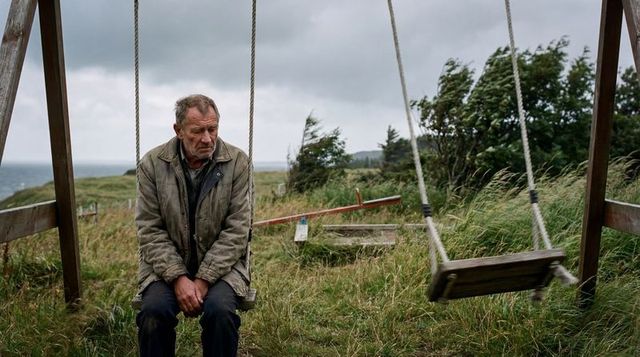 Sitting elderly man on swing at windswept coastal bluff contemplating solitude and loss