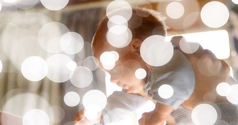 Cradling infant in striped onesie with warm bokeh backlight and cozy caregiver embrace