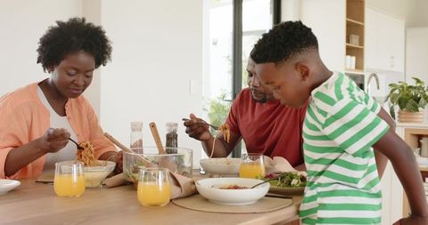African american family sharing relaxed pasta meal at kitchen table with orange juice