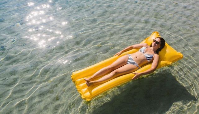 Woman relaxing on yellow inflatable float in clear shallow sea wearing sunglasses