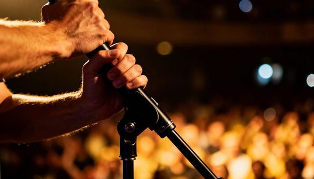 Performer gripping microphone stand on stage with warm bokeh crowd lights