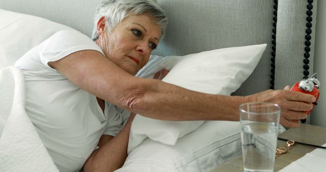 Senior Woman Reaching for Alarm Clock in Bed in Morning - Download Free Stock Images Pikwizard.com