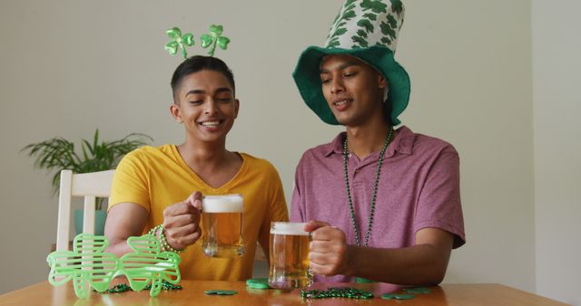 Biracial gay male couple making st patrick's day image call raising glasses wearing costumes. staying at home in isolation during quarantine lockdown.