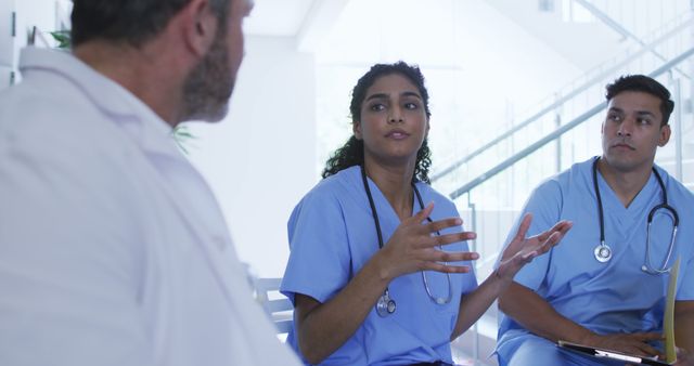 Medical professionals in blue scrubs discuss patient care during a meeting. Suitable for content about healthcare teamwork, communication in medical fields, and hospital environment. Can be used in medical articles, healthcare advertising, and training materials.