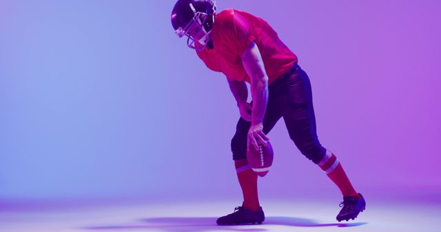 Image of caucasian american football player in helmet with ball kneeling over neon purple background. American football, sports and competition concept.